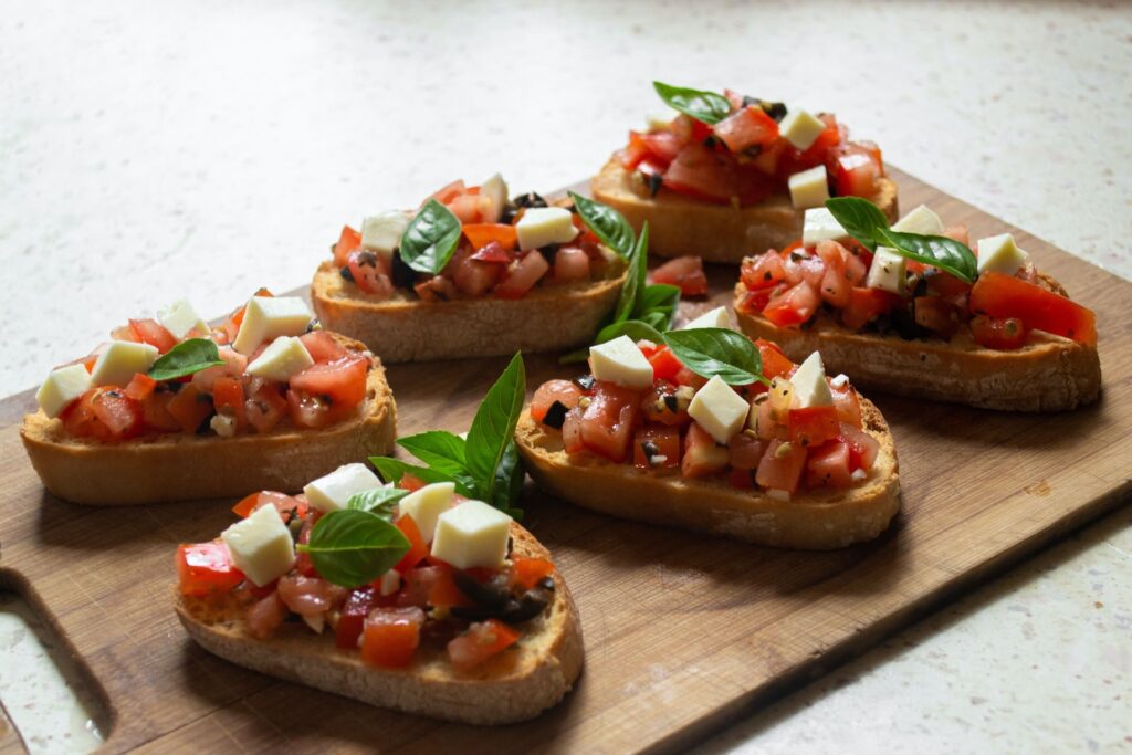 Bruschetta topped with diced tomatoes, mozzarella cubes, and fresh basil leaves arranged on a wooden board, creating an inviting, fresh appetizer.